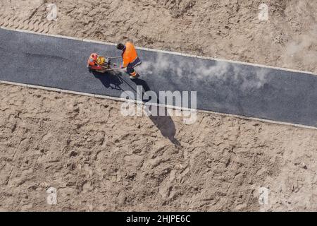 Asfalto caldo pavimentazione stradale costruzione cantiere uomo compattatore a piastre vibranti Rammer. Nuovo operatore di costruzione stradale che stesa la superficie di asfalto sulla passerella Foto Stock