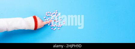 Pillole rosa su sfondo blu con un cuore al centro. Concetto di salute del cuore. La mano dei bambini mostra un cuore tra le pillole rosa. Foto Stock