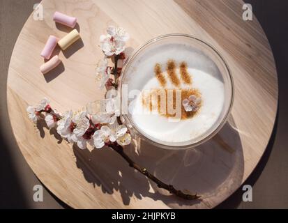 Fiore primavera ramo vicino a una tazza di caffè con un motivo di cannella su schiuma di latte su un supporto rotondo di legno. Vista dall'alto. Pensiero positivo, buono Foto Stock
