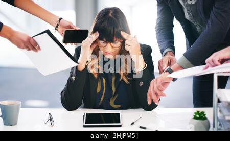 Quando è sufficiente, basta. Scatto di una giovane donna d'affari che guarda stressata mentre è sopraffatta dalle richieste dei suoi colleghi in un ufficio moderno. Foto Stock