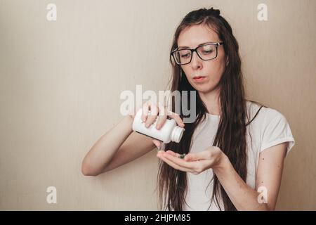 Una ragazza con capelli lunghi e bicchieri si versa capsule di spirulina da un vaso. Vitamine verdi in forma di capsula. Superfood per la salute delle donne. Vitamine Foto Stock