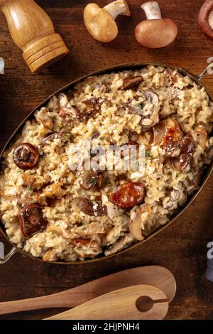 Risotto ai funghi, riso rustico ai funghi, con ingredienti, sparato dall'alto su sfondo di legno scuro Foto Stock