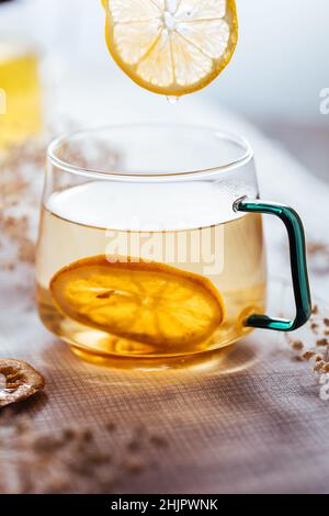 Tazza di tè alla camomilla in tazza trasparente servita con fetta di limone e arancia. Pausa tè. Foto Stock