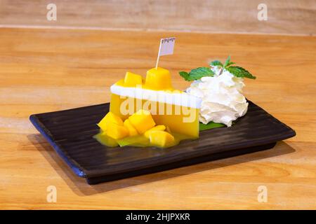 Dessert di gelatina di budino di mango su sfondo nero piatto di legno primo piano, mousse di mango con mango mature affettate sul lato, fuoco selettivo Foto Stock