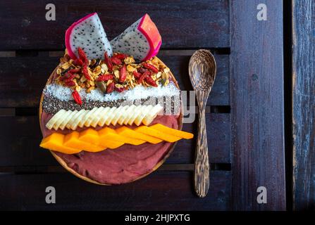 Ciotola per frullati con semi di chia, muesli, fragole, fette di banana e fiocchi di cocco, vista dal tavolo. Colazione salutare Foto Stock