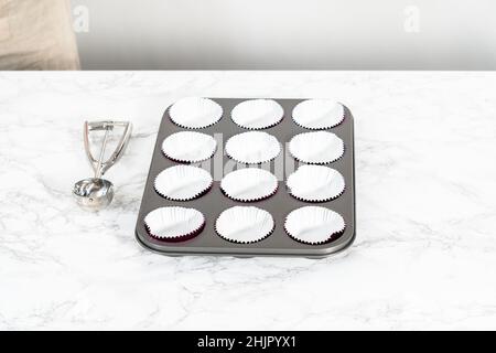 Cottura di cupcake al cioccolato. Fodera teglia per cupcake in metallo con fodere per cupcake. Foto Stock