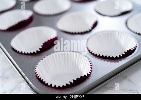 Cottura di cupcake al cioccolato. Fodera teglia per cupcake in metallo con fodere per cupcake. Foto Stock