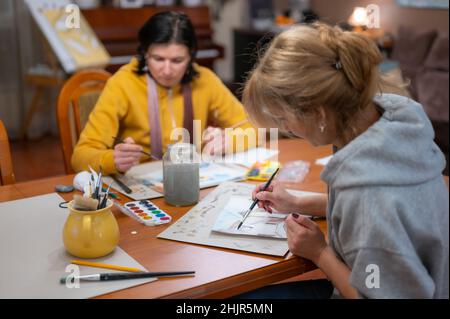 Processo di laboratorio di arte creativa. Due artisti giovani donne che dipingendo colorato paesaggio urbano su carta utilizzando pennello e acquerelli Foto Stock