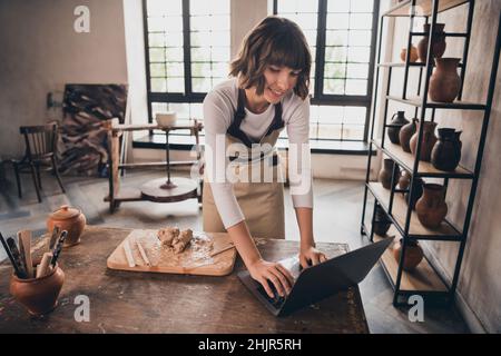 Foto di focalizzato self-used donna vasaio ispirato modellare stoviglie ricerca netbook webinar in sala di lavoro Foto Stock