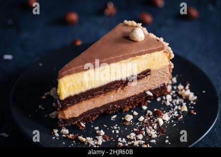 Torrone la vaniglia e la torta glassata al cioccolato in quattro strati con le nocciole sulla parte superiore e le nocciole sbriciolate intorno su uno sfondo scuro Foto Stock