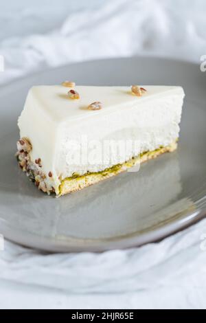 Torta a quattro strati con pistacchio, vaniglia e cioccolato bianco su piatto grigio con pistacchi in cima Foto Stock