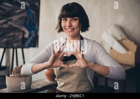 Foto di self-empowered signora piccolo negozio proprietario vasaio fare cuore forma godere vita vocazione hobby sedersi in sala di lavoro Foto Stock