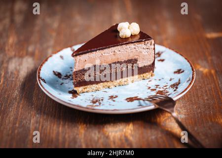 Torta di nocciole al cioccolato con cinque strati di biscotto e crema con glassatura al cioccolato sulla parte superiore e noci intere piemontesi. Servita e decorata con cof Foto Stock