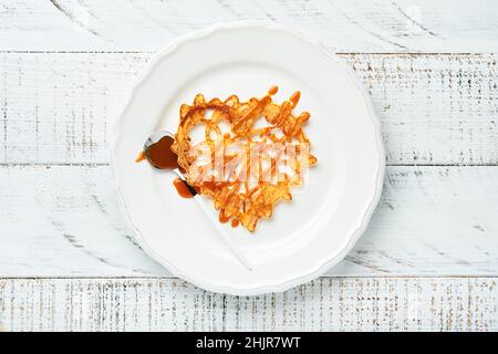 Frittelle o crepes a forma di cuore cosparse di caramello su piatto bianco su vecchio sfondo rustico. Impostazione della tabella per il vostro giorno di San Valentino preferito br Foto Stock