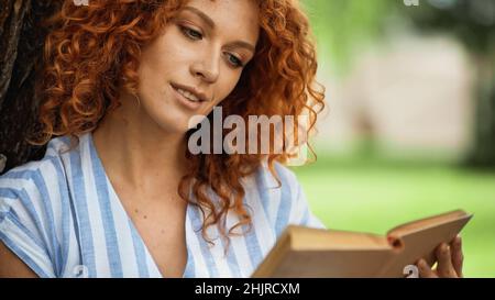 curly redhead donna lettura libro nel parco Foto Stock