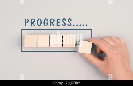Le parole Progress stanno in piedi sopra la barra di caricamento, mano mette l'ultimo cubo per il caricamento, sfondo grigio Foto Stock