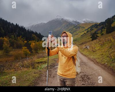 L'uomo crea splendide foto sullo smartphone per i social network. Stile di vita vagante, concetto di avventura vacanza autunnale all'aperto, da solo in natura. Viaggia verso il Caucaso settentrionale, Arkhyz, Russia Foto Stock