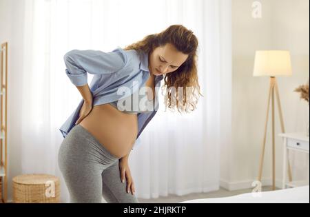 Giovane madre futura che soffre di dolore nella sua parte inferiore stanca della schiena durante la gravidanza Foto Stock