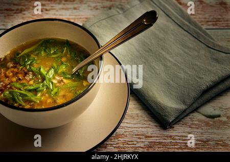 Zuppa con lenticchie e cipolle verdi su brodo di pollo in un recipiente bianco su un tavolo retrò in legno Foto Stock