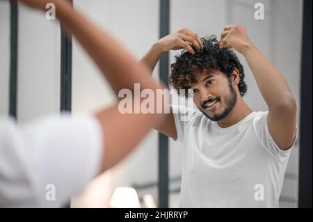 Felice ragazzo messo a fuoco styling i suoi capelli ricci con mousse schiuma Foto Stock