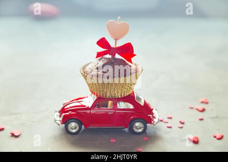 L'auto retrò rossa porta un cupcake al cioccolato con una candela a forma di cuore. Carta romantica per San Valentino. San Pietroburgo, Russia - 31 gennaio 2022 Foto Stock