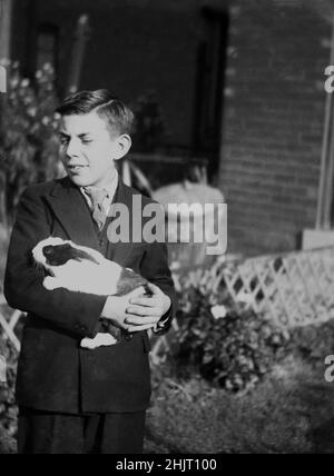 1940s, storico, un ragazzo adolescente in abito a due razze, in piedi fuori tenendo il suo animale domestico porcellino d'India, Dudley, Warwick, Inghilterra, Regno Unito. Originari del Sud America, i maiali della Guinea sono stati portati in Europa e dal 1800s sono stati animali domestici popolari. Foto Stock