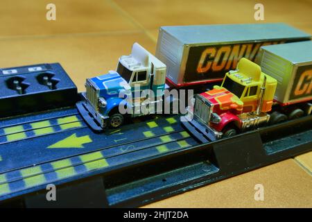 Immagine di piccoli camion con cabine multicolore all'uscita di un circuito giocattolo installato sul pavimento della stanza dei bambini Foto Stock