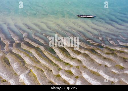 In inverno il livello dell'acqua del fiume Jamuna scende molto lasciando enormi sabbie sul letto del fiume. Nella foto un pescatore sta navigando la sua barca attraverso la corrente lenta del fiume. Foto Stock