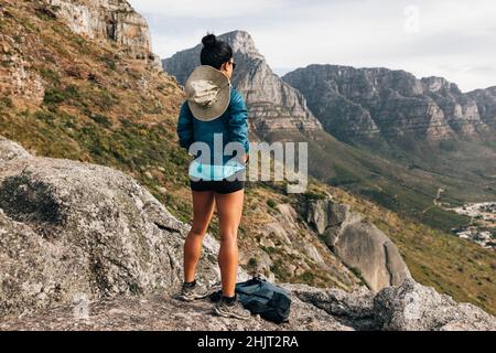 Vista posteriore di una donna escursionista che guarda la vista da una cima di montagna. Donna che prende una pausa dopo una salita. Foto Stock