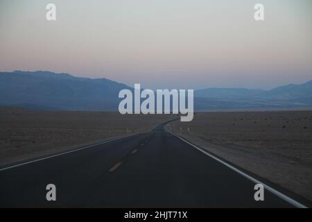 La strada che non finisce mai durante il tramonto nel deserto della Death Valley in California Foto Stock