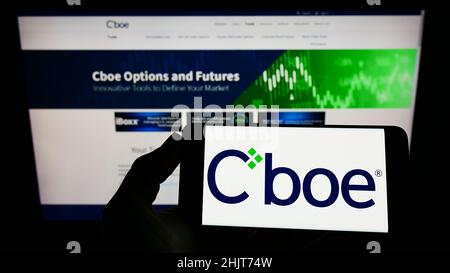 Persona che tiene uno smartphone con il logo della società finanziaria statunitense CBOE Global Markets Inc. Sullo schermo di fronte al sito Web. Mettere a fuoco sul display del telefono. Foto Stock