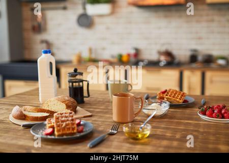 Immagine di sfondo di dolci waffle da colazione con fragola su tavolo in legno in una cucina accogliente, spazio copia Foto Stock