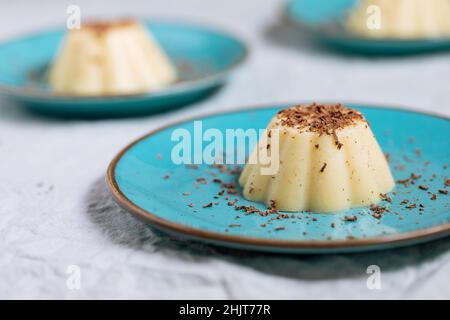 Budino di vaniglia su piastra di porcellana blu con briciole di cioccolato sulla parte superiore. Sfondo luminoso Foto Stock