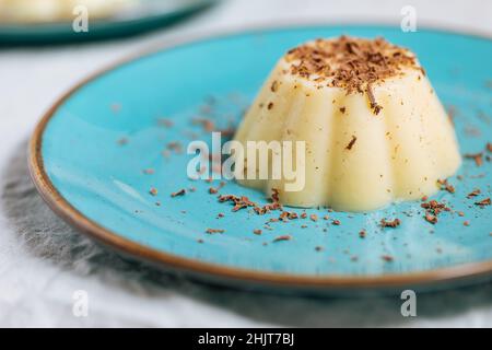 Budino di vaniglia su piastra di porcellana blu con briciole di cioccolato sulla parte superiore. Sfondo luminoso Foto Stock