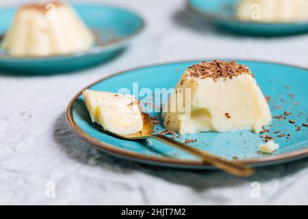 Budino di vaniglia su piastra di porcellana blu con briciole di cioccolato sulla parte superiore. Sfondo luminoso Foto Stock