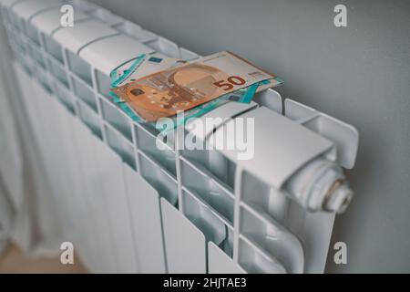 Pagamento delle fatture. Banconote in euro sulla batteria del radiatore di riscaldamento a casa. Costi di riscaldamento costosi, risparmio energetico nella stagione invernale Foto Stock