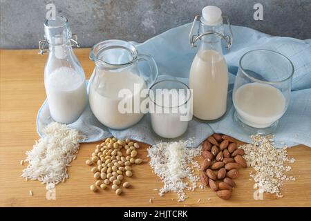 Varie alternative di latte vegano da riso, soia, cocco, mandorla e avena in bottiglie e bicchieri su un tavolo di legno, fuoco selezionato, stretta profondità di fie Foto Stock