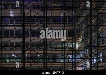 Costruzione di ponteggi in ferro attorno a un moderno edificio in acciaio e vetro per uffici di notte Foto Stock