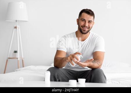 Felice caucasico giovane attraente utilizza crema idratante della pelle e lozione anti-invecchiamento Foto Stock