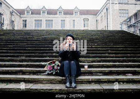 Donna asiatica si è seduta sui passi facendo le foto a Winchester, Regno Unito Foto Stock