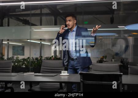 Un uomo d'affari furioso che cammina in ufficio mentre si fa una telefonata Foto Stock