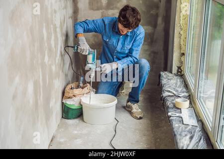 Giovane maschio pittore massaggia putty con acqua in un secchio con un hand-held mixer per mix di costruzione Foto Stock