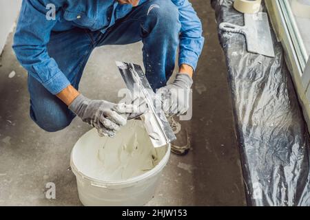 Master è l'applicazione di stucco bianco su una parete e macchie da coltello da stucco in una stanza per restauro di casa in ore diurne Foto Stock