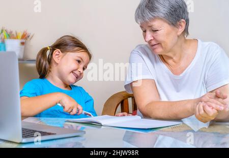 La nonna aiuta il bambino a studiare online di fronte al laptop Foto Stock