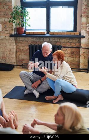 Coppia anziana seduta su materassino da sforzo e uso del telefono cellulare insieme durante la lezione di yoga nel centro benessere Foto Stock