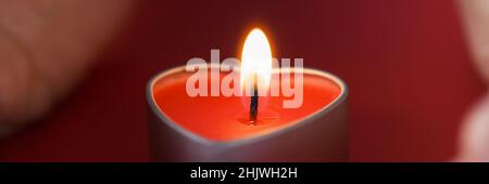 Le mani femminili che tengono una candela a forma di cuore in primo piano scuro Foto Stock