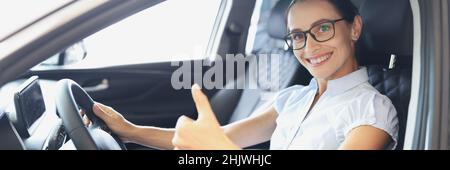 Ritratto di donna sorridente che guida la nuova macchina mostra pollici in primo piano Foto Stock