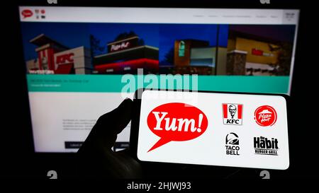 Persona che tiene smartphone con il logo della società americana di fast food Yum! Brands Inc. Sullo schermo di fronte al sito Web. Mettere a fuoco sul display del telefono. Foto Stock