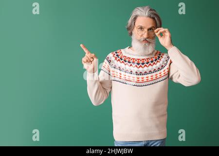 Bell'uomo anziano in maglia maglione che punta a qualcosa su sfondo verde Foto Stock