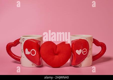 Due tazze abbinate con l'iscrizione Love e un cuore rosso peluche tra loro Foto Stock